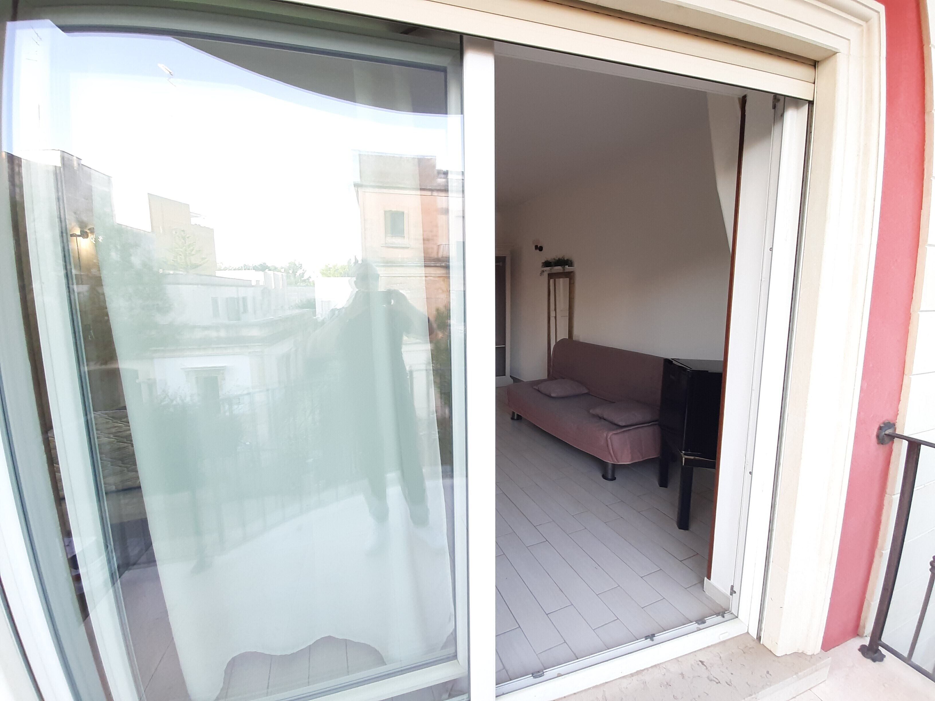 A balcony with a sliding glass door, a sofa, and a floor lamp.