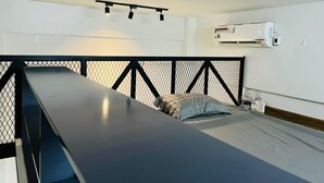 Ein Einzelbett mit schwarzem Metall-Kopfstück, eine weiße Klimaanlage an der Wand und eine Deckenleuchte.