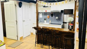 Ein kompakter Küchenbereich mit Bar und Barhocker, einem Kühlschrank und einem 'Happy Birthday India'-Banner.