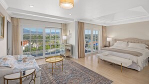 Un dormitorio amplio con una cama grande, un sofá, una mesita y vistas a la ciudad a través de grandes ventanales.