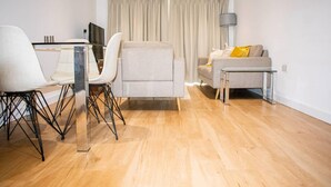 A modern living room with a sofa, a glass coffee table, and a dining area with chairs and a table. - London - Apartment - Sleeps 2 - Garden - Pool (London)
