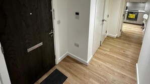 A hallway with wooden flooring, a black doormat, and white walls. - London - Apartment - Sleeps 2 - Garden - Pool (London)
