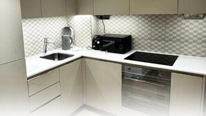 A modern kitchen with a white countertop, a coffee maker, a microwave, and a dishwasher. - London - Apartment - Sleeps 2 - Garden - Pool (London)