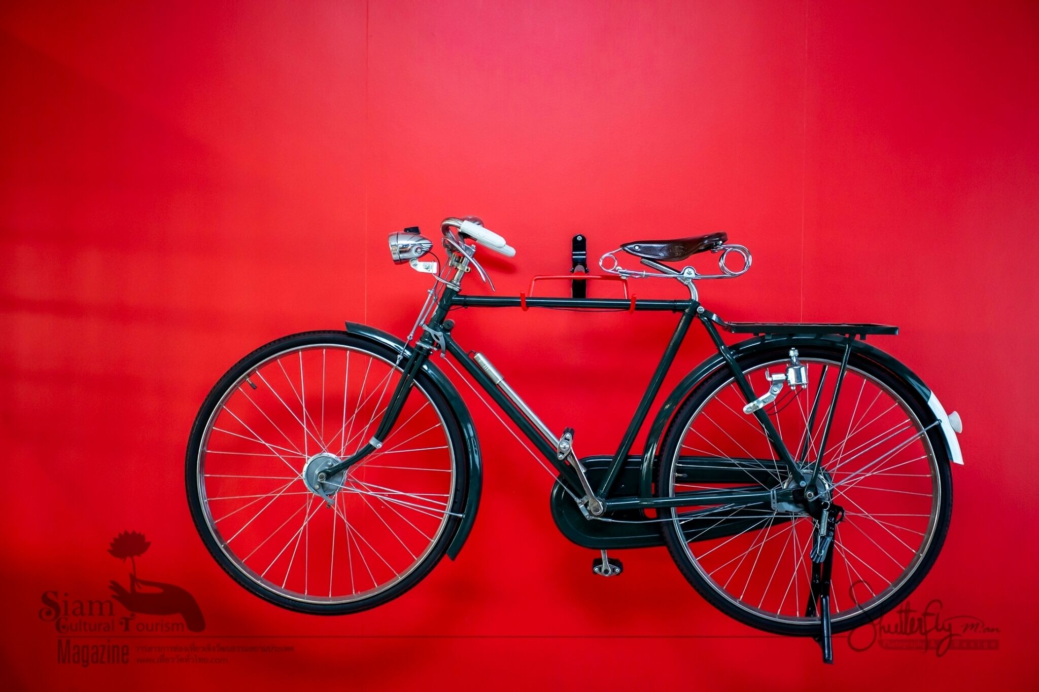 Una bicicleta negra con asiento y manillar blancos, colgada de una pared roja.