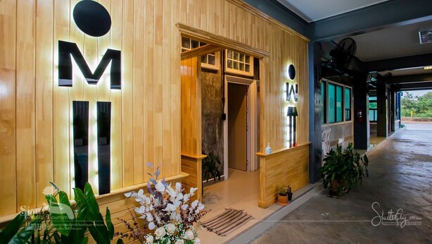 A wooden exterior with illuminated 'M' and 'A' signs, a reception desk, and potted plants. - Thaphon Residence (Phetchabun)