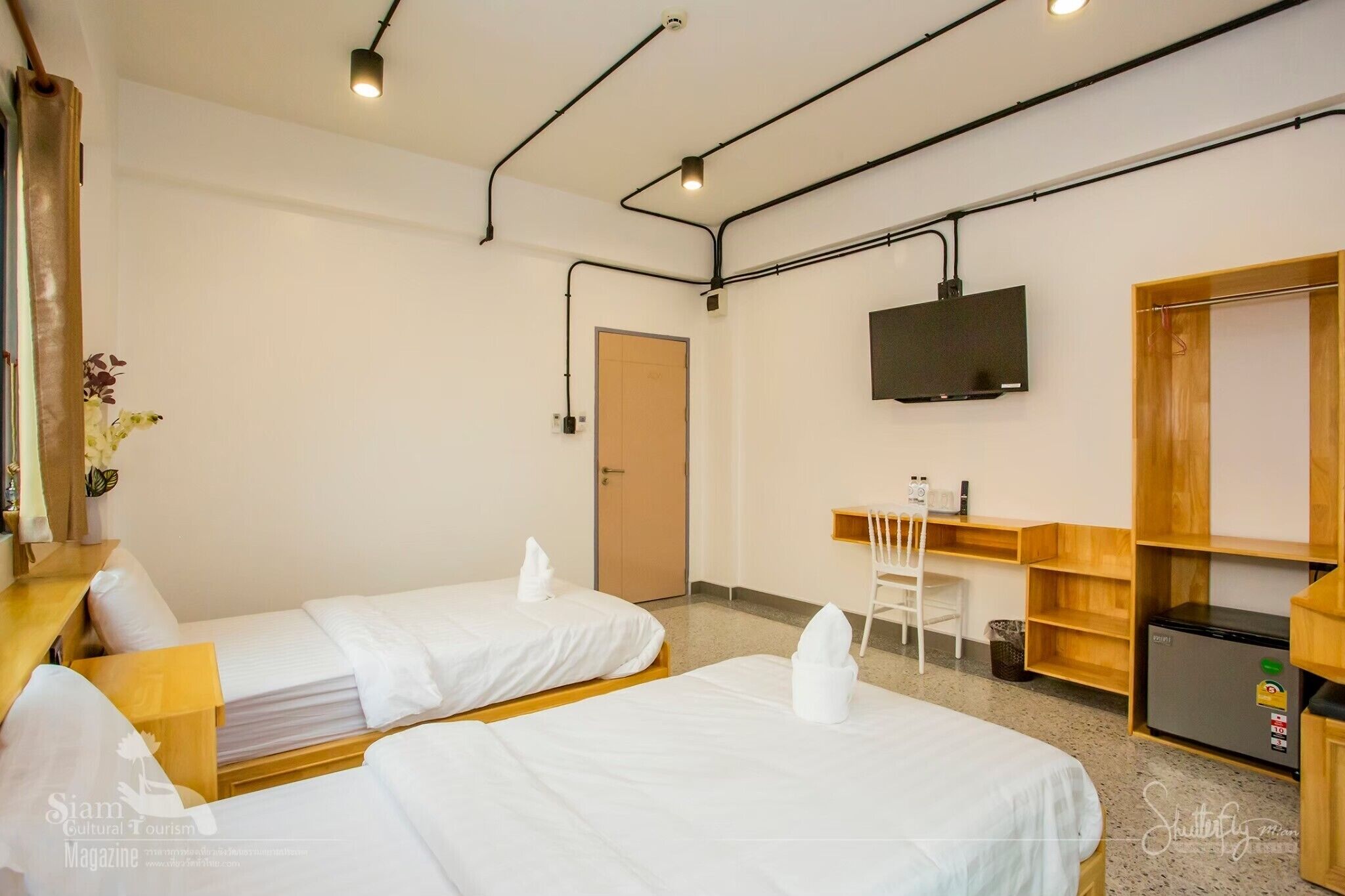 A hotel room with two beds, a desk, a chair, a TV, and a wardrobe.