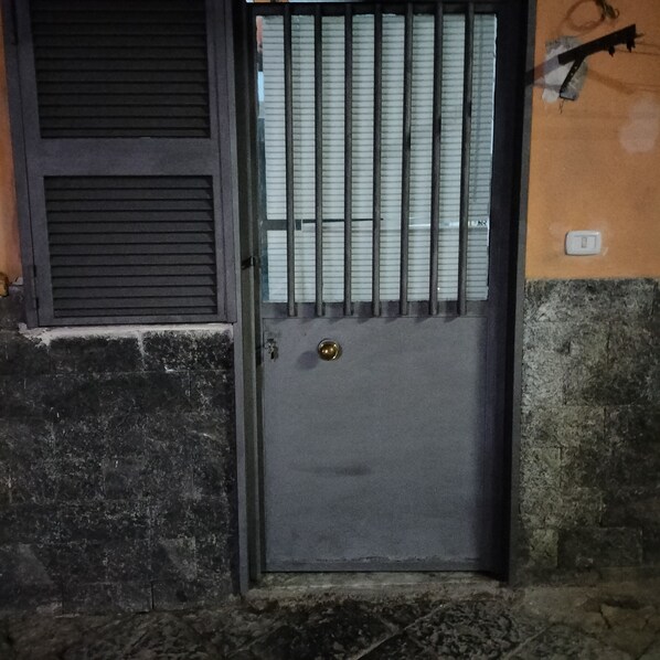 A dark-colored door with a metal gate, a window with horizontal blinds, and a wall with a rough texture. - G&G small cozy facility,,5 minutes away from the wonderful forest (Napoli)