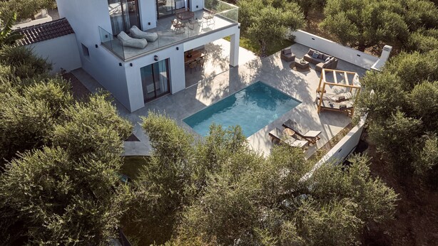 Et moderne hus med to etager og en pool, omgivet af frodig vegetation.