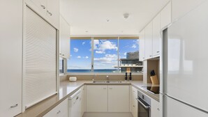 Une cuisine moderne avec vue sur l’océan, dotée de meubles blancs, d’un four encastré et d’une grande fenêtre.