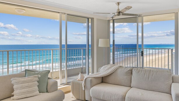 Un balcon avec vue sur l’océan, un ventilateur de plafond et un canapé agrémenté de coussins.