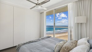 Une chambre à coucher avec un lit, un ventilateur de plafond, une vue sur la plage et une fenêtre avec des rideaux.