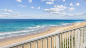Vue sur la plage depuis un balcon doté d’une balustrade, avec l’océan et le rivage au loin.