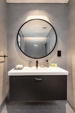 A modern bathroom with a round mirror, white sink, and dark cabinetry.