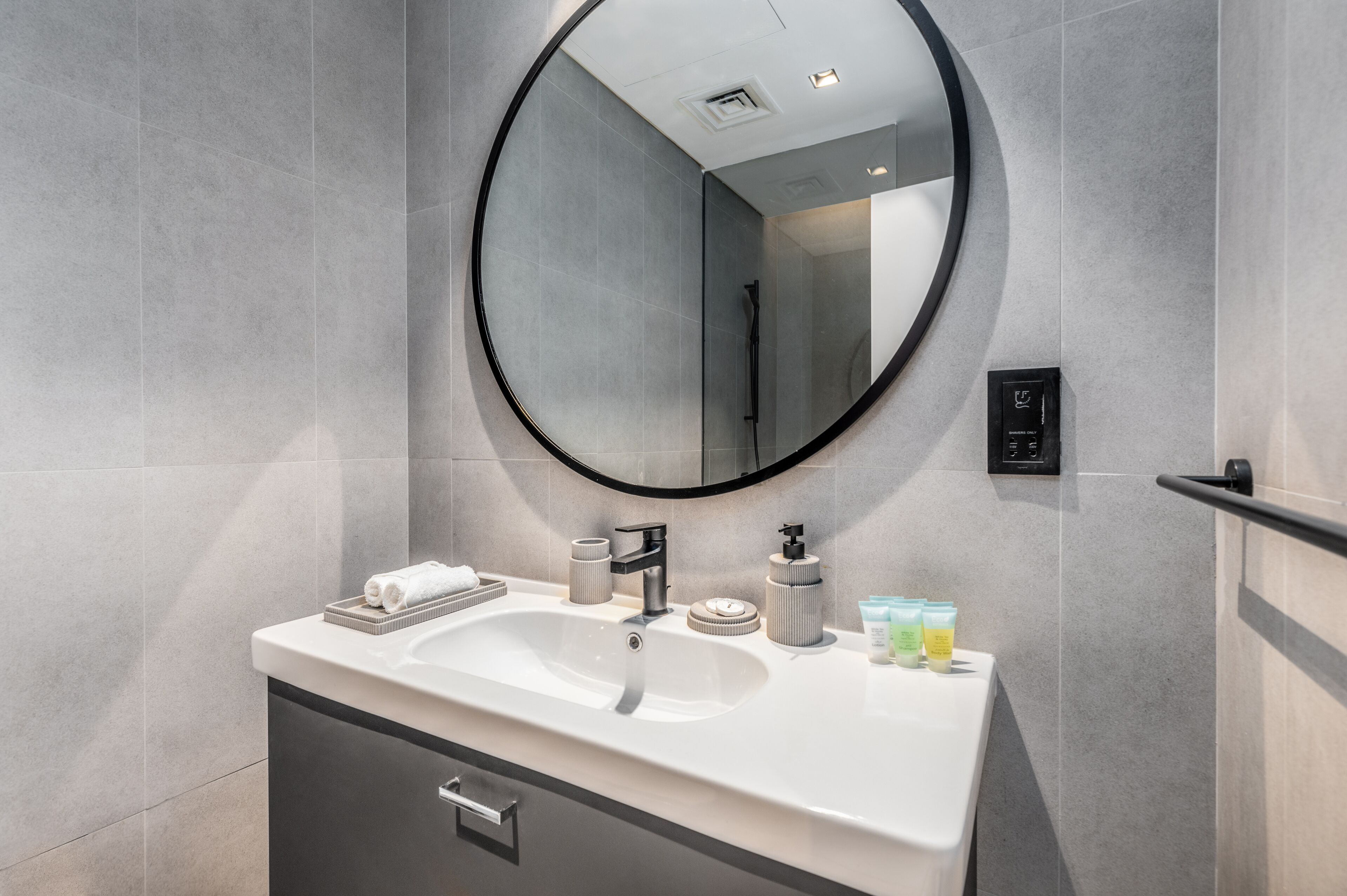 A modern bathroom with a large mirror, a white sink, and toiletries on the counter.
