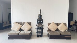 A room with two sofas, each with floral cushions, a small table with a statue, and a plain white wall. - Siam Villa Suvarnabhumi (Bangkok)