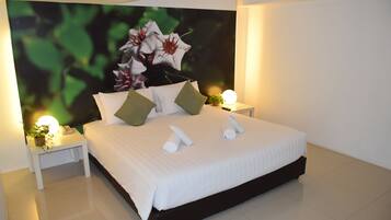 A modern hotel room with a large bed, two bedside tables, a nightstand, a wall-mounted TV, and a potted plant.
