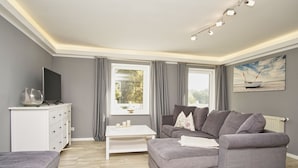 Un salon moderne avec un canapé gris, une table basse blanche et un téléviseur posé sur un meuble blanc.