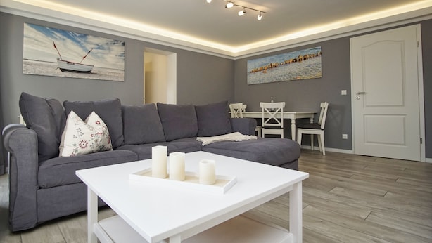 Un salon moderne avec un canapé gris, une table basse blanche et des tableaux accrochés aux murs.