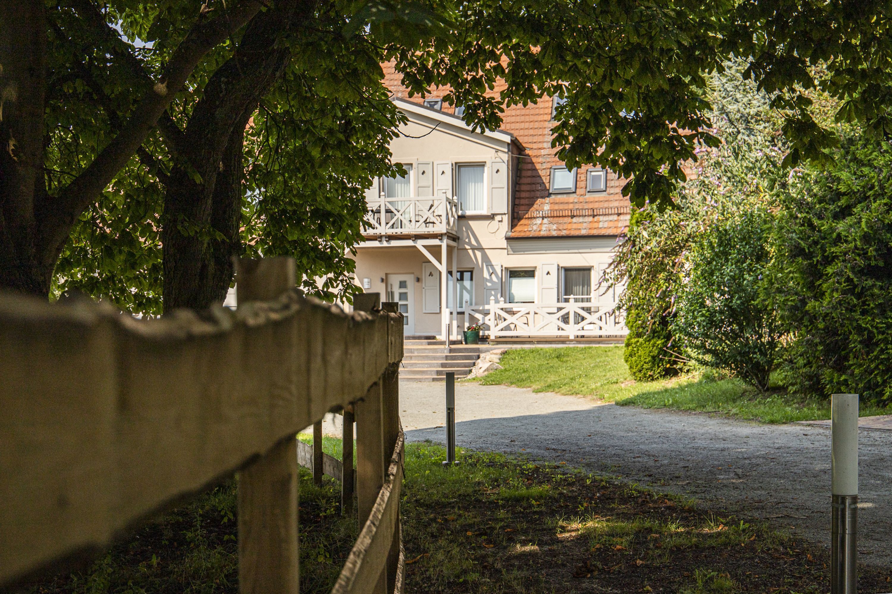 A building with a balcony, a gravel driveway, and a wooden fence.