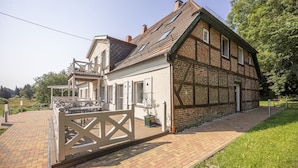 Une maison traditionnelle à colombages, avec une façade en briques, une terrasse en bois et un portail blanc.
