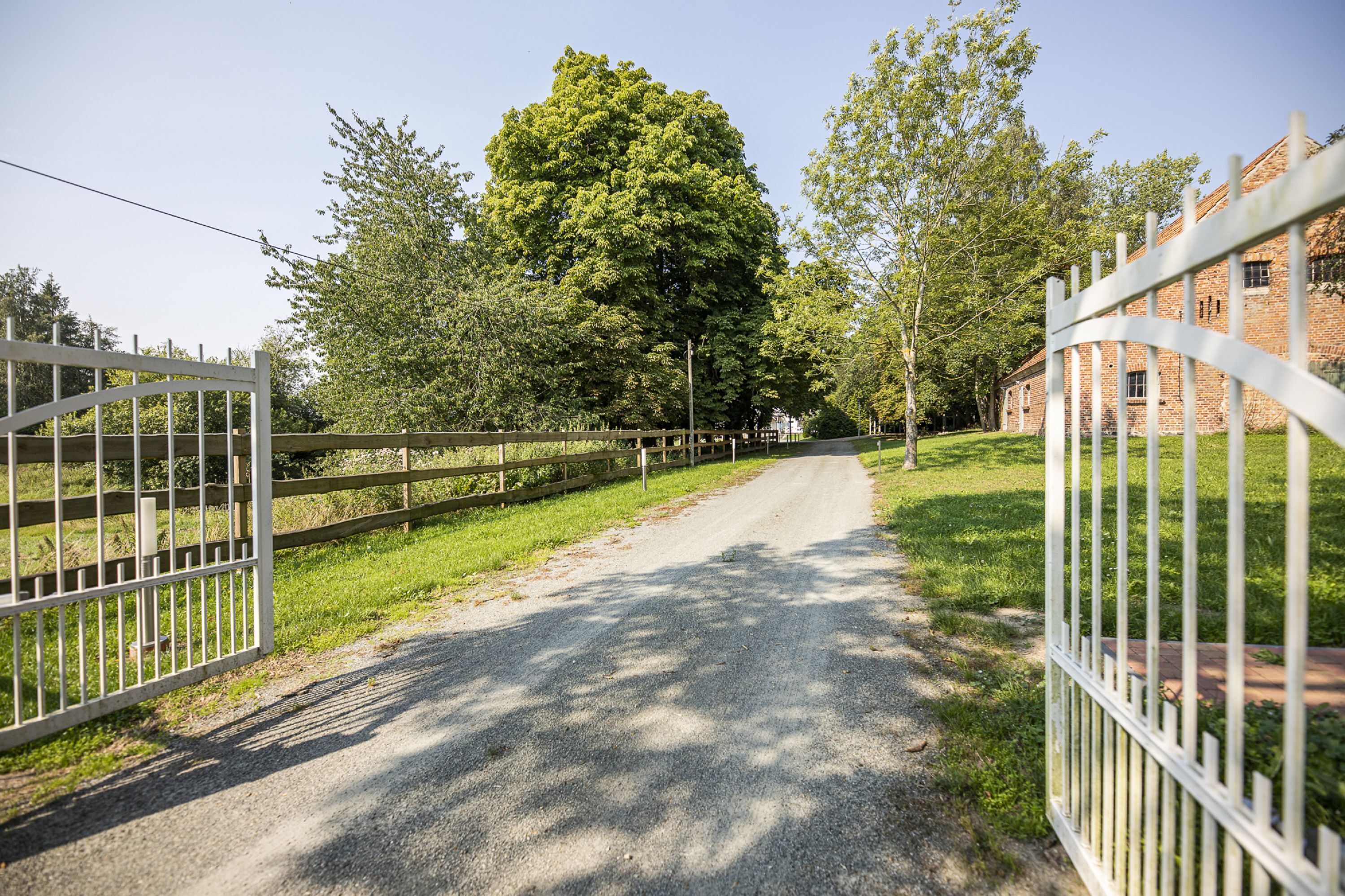 A gravel path flanked by white metal gates leading to a building with a brick facade.