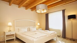 A bedroom with a white bed, two bedside tables with lamps, a floor lamp, a window with curtains, and wooden ceiling beams. - Ruhig und Idyllische Lage im Herzen der Insel Rügen - Gutshaus Silvitz Fewo 04 (Bergen auf Rügen)