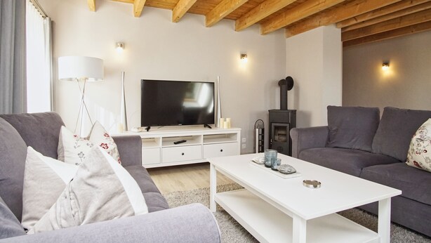 A modern living room with a wooden ceiling, grey sofas, a white coffee table, a flat-screen TV, and a fireplace. - Ruhig und Idyllische Lage im Herzen der Insel Rügen - Gutshaus Silvitz Fewo 04 (Bergen auf Rügen)