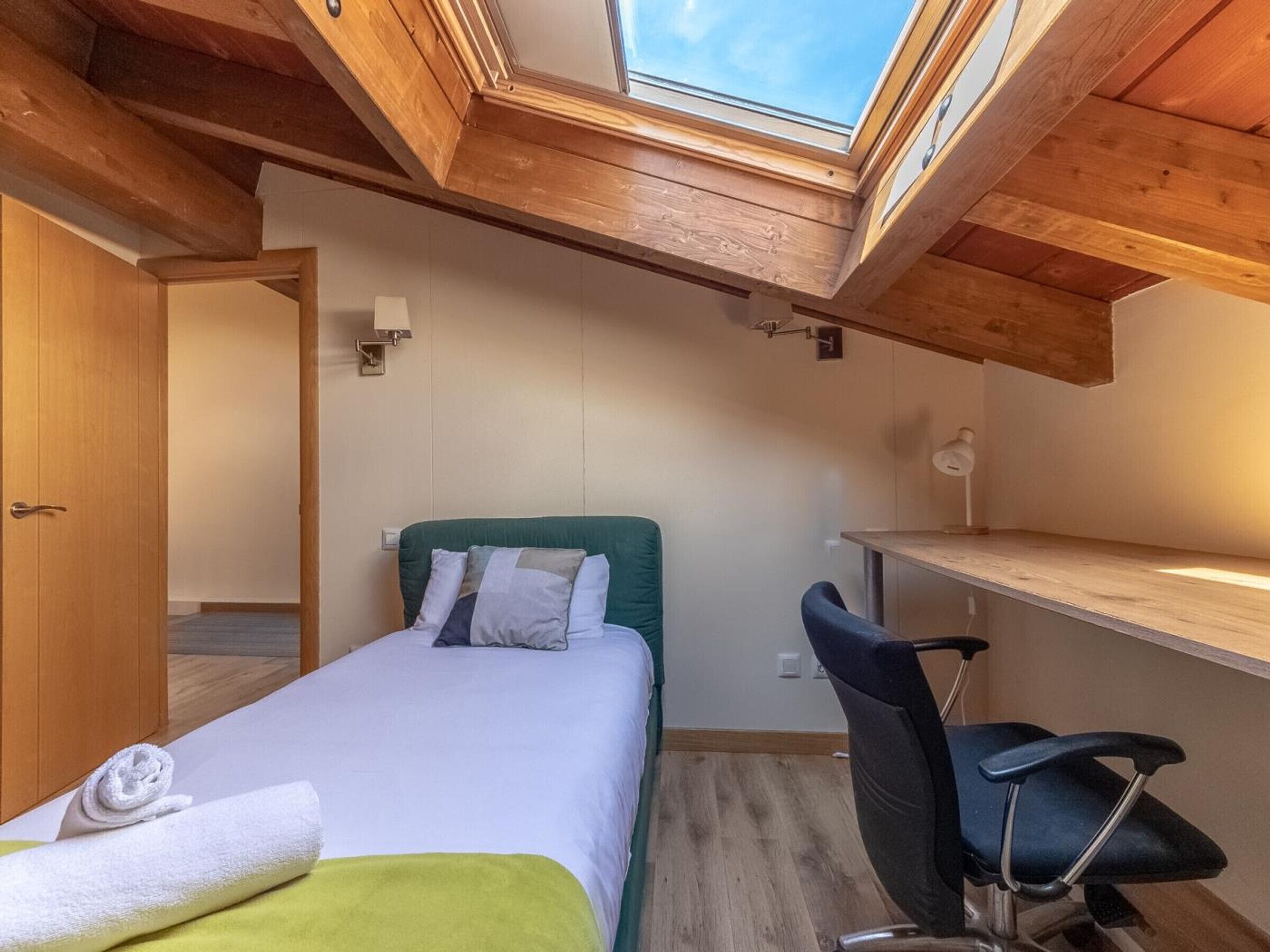 Ein kleines Schlafzimmer mit Oberlichter, einem Bett mit Kissen, einem Schreibtisch und einem Stuhl.