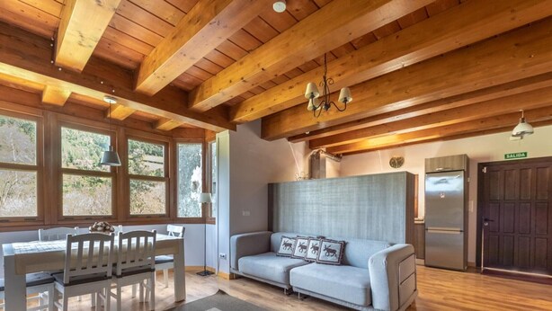 Una habitación acogedora con techo de madera, un sofá con cojines de motivos animales, una mesa de comedor con sillas y un refrigerador.