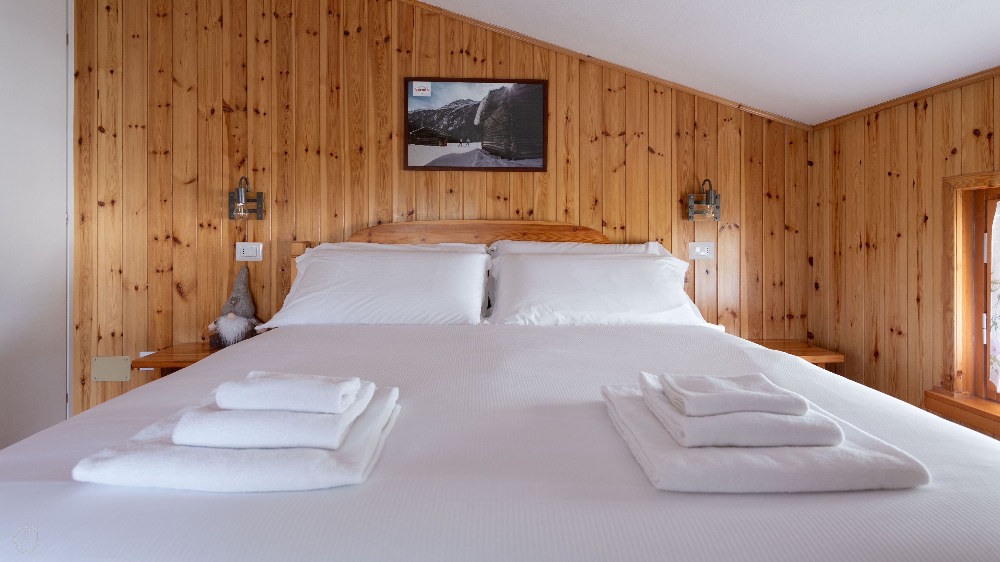 A wooden-paneled bedroom with a bed, pillows, and a framed picture on the wall.