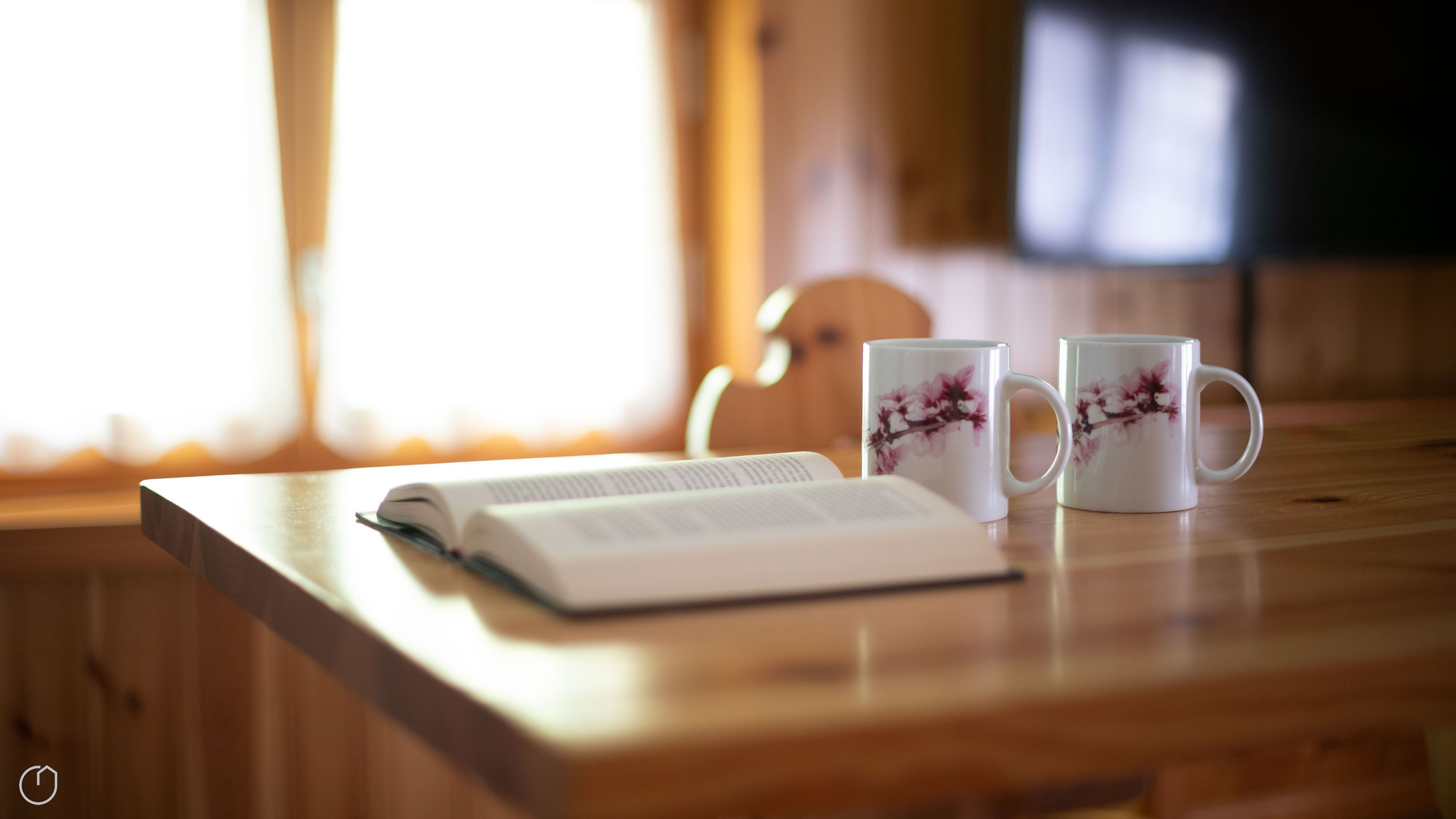 A wooden table with an open book and two white mugs with floral designs.