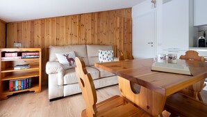 Una sala de estar acogedora con pared de madera, un sofá, una mesa de centro de madera y una estantería llena de juegos de mesa.