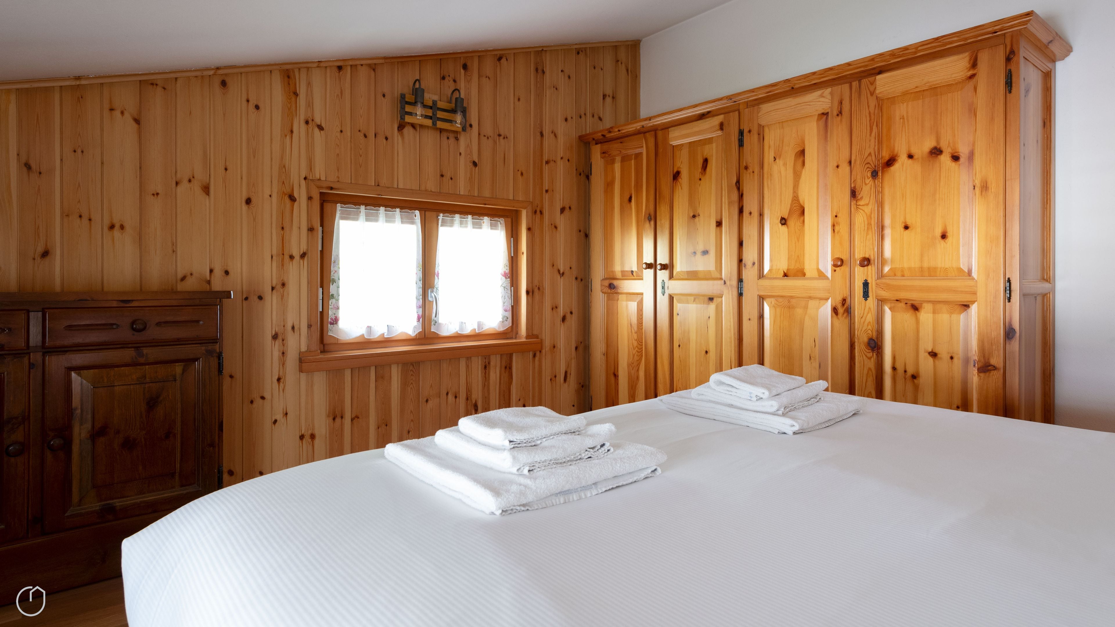 A wooden-paneled room with a bed, a window, and a wardrobe.
