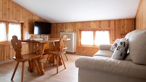 Una habitación con paneles de madera, una mesa de comedor, sillas, un sofá y un televisor.