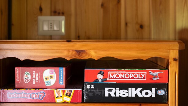 A wooden shelf with four board games: Uno, Monopoly, Indovina, and Risiko. - Leopardi 3 (Bormio)