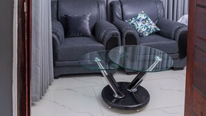 Ein modernes Wohnzimmer mit zwei Ledersofas, einem Glastisch und grauen Vorhängen.