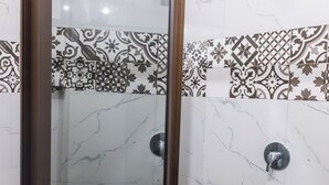 Eine gläserne Dusche mit Marmorwand und gemusterten Fliesen.