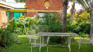 Un conjunto de mesa y sillas metálicas en un jardín exuberante, con un edificio de ladrillo al fondo.