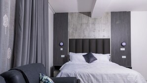 Ein modernes Hotelzimmer mit einem großen Bett, einem dunklen Sessel und einem Nachttisch.