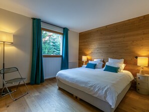 Ein Schlafzimmer mit einem Bett, Nachttischlampen, einem Sessel und einem Fenster mit Vorhängen.