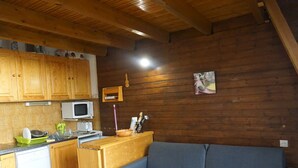 Eine kompakte Küche mit Holzschränken, einer Mikrowelle und einem Geschirrspüler. Ein blaues Sofa steht an der Wand, und ein kleines Regal beherbergt Küchenutensilien.