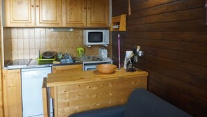 Eine kleine Küche mit Holzschränken, einer Mikrowelle und einer Arbeitsplatte mit verschiedenen Küchenutensilien.