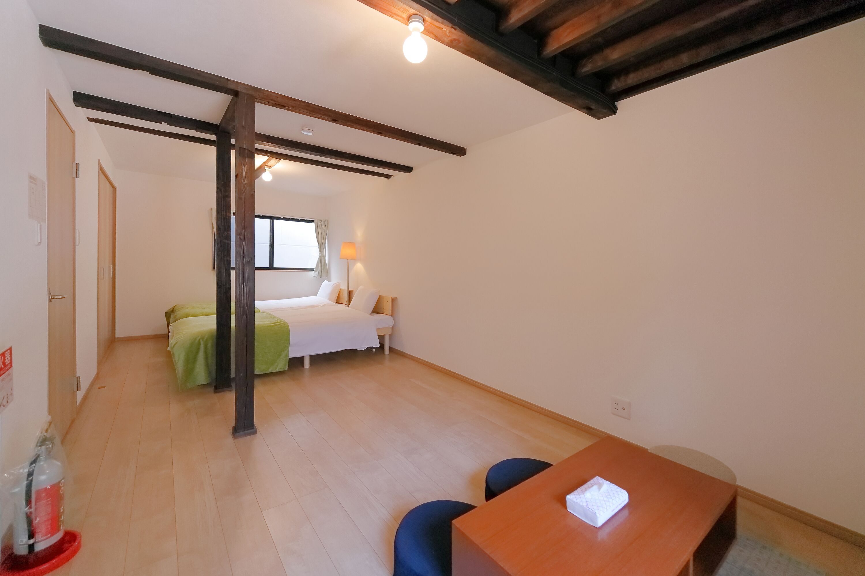 A room with a bed, a table, and a chair. There is a window with a view of the outside.