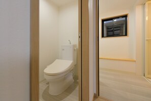 A small, clean bathroom with a toilet, a window, and a wooden door.