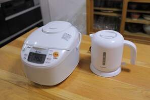 A white rice cooker and a white electric kettle on a wooden table.