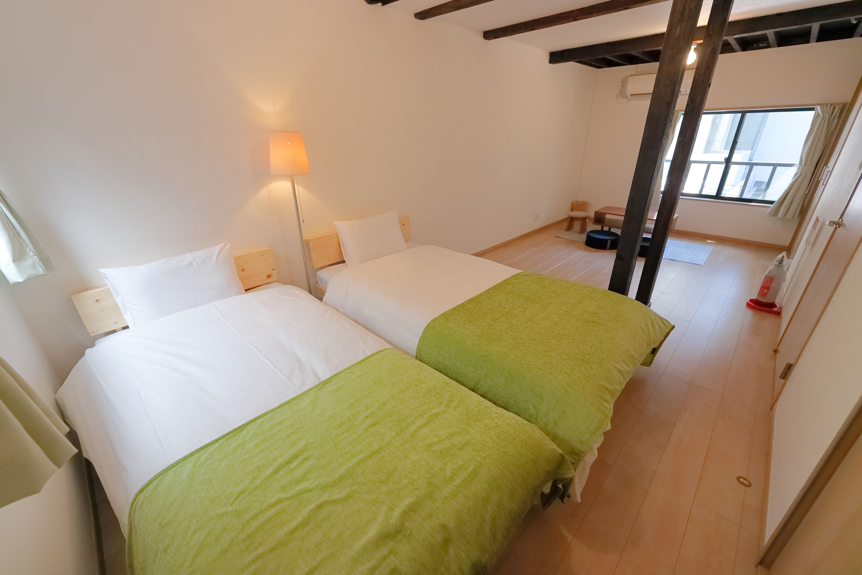 A hotel room with two beds, a nightstand, a lamp, and a window with curtains.