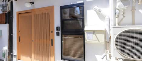 A building with a wooden door, a window with blinds, and an air conditioning unit.