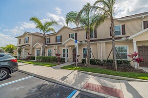 Un edificio residencial de varios pisos con estacionamiento, palmeras y señal de acceso para personas con discapacidad.