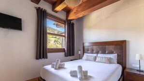 A hotel room with a large bed, wooden headboard, and a window with curtains.