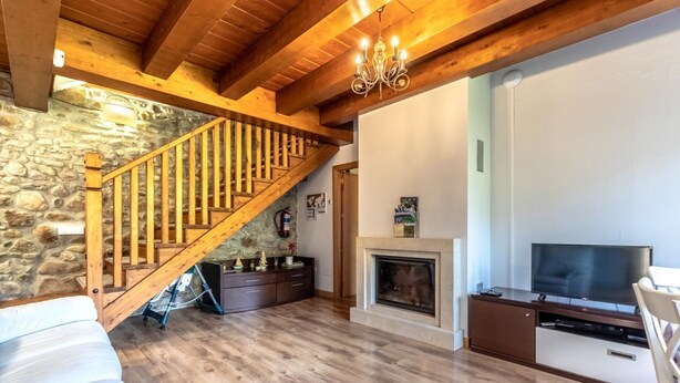 A cozy living room with a stone wall, wooden staircase, fireplace, and a flat-screen TV.